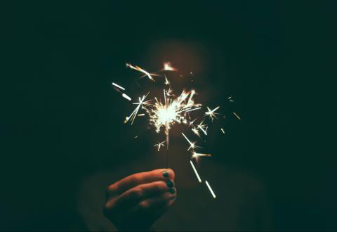 Illustration. A hand is holding a sparkler in the dark.