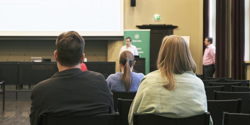 En bild av publiken vid ett evenemang för öppen vetenskap. I förgrunden två personer vända mot scenen med ryggen mot kameran. 