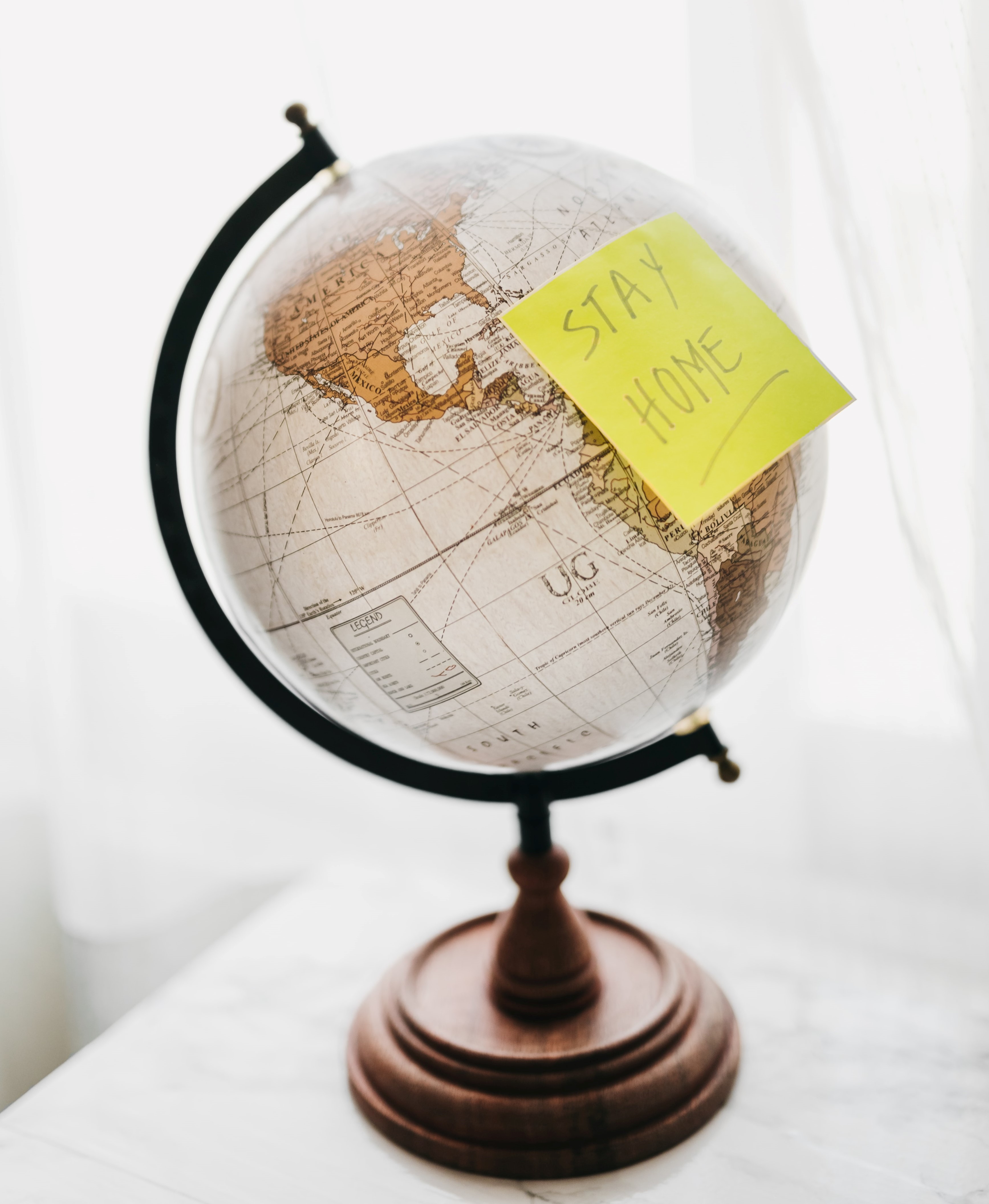 The image has a globe with a post it sticker on it that reads stay home.